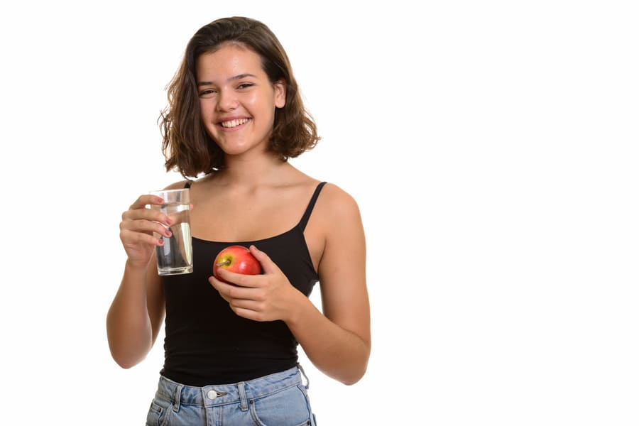 young-happy-caucasian-teenage-girl-smiling-while-holding-glass-water-red-apple (1).jpeg