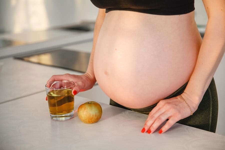 pregnant-woman-with-bare-stomach-stands-near-table-with-apple-juice-her-hands (1).jpeg