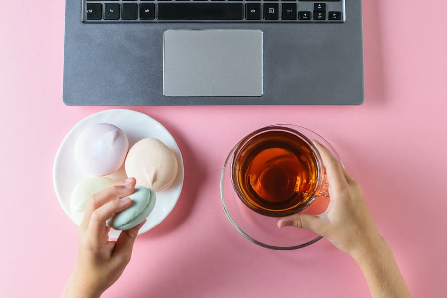 girl-eats-colored-marshmallows-drinks-tea-near-computer-pink-table-view-from-top (1).jpeg