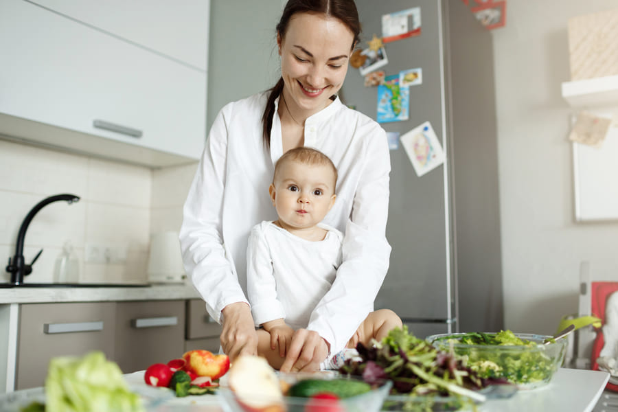 young-happy-mother-cooking-food-kitchen-taking-care-baby (1).jpeg