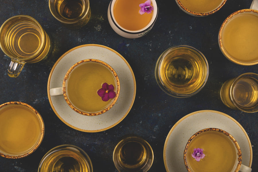 many-different-cups-tea-with-violet-flowers-dark-blue-background-top-view-layout (1).jpeg