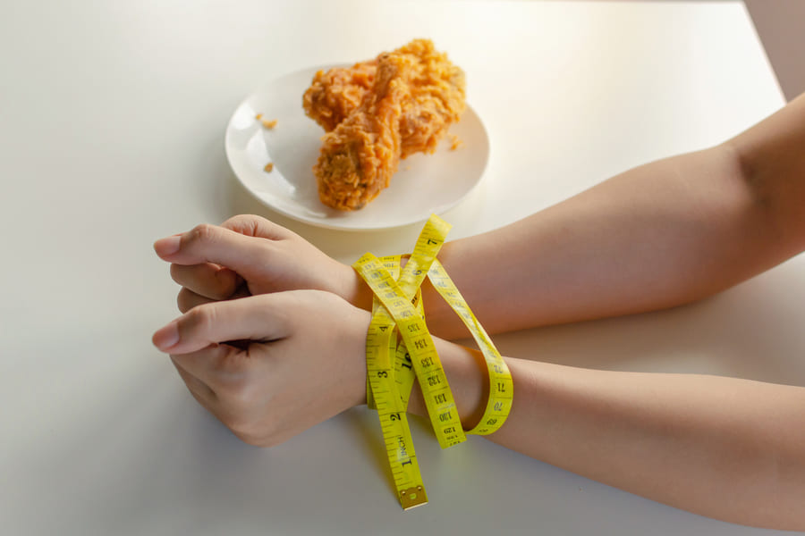 diet-young-woman-slim-body-hands-tied-with-yellow-measuring-tape-delicious-crispy-fried-chicken-dish-desk-kitchen-home (1).jpeg